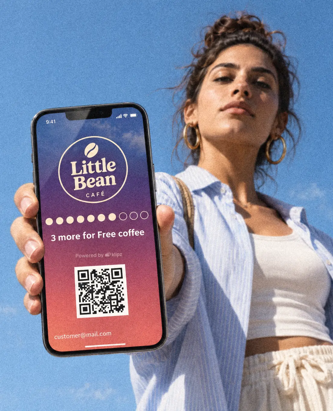 A woman under a blue sky holds out her phone, her Little Bean membership open on the screen.